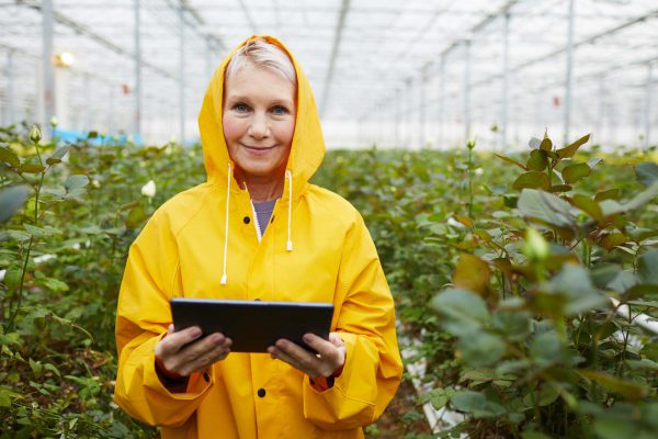 A woman monitors the humidity levels of her greenhouse using IoT software on her tablet.