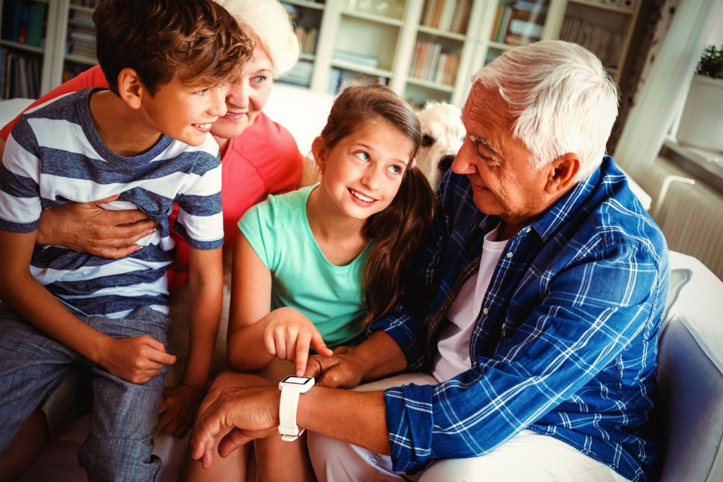 A man shows his grandchildren the IoT human fall sensor that he wears on his wrist.
