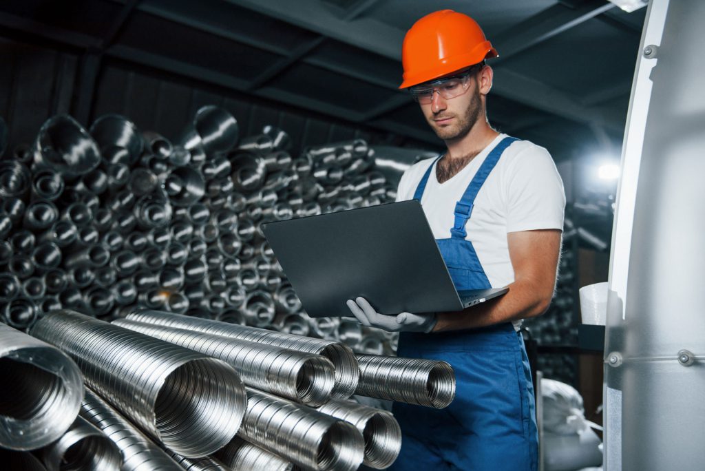 A factory worker measures the duct supply using IoT software on his laptop.