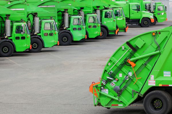 Multiple waste management trucks that are tracked using IoT asset trackers are parked in a lot.