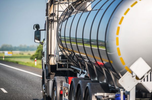 A tanker truck that is monitored with IoT tank level sensors moves down a country road.