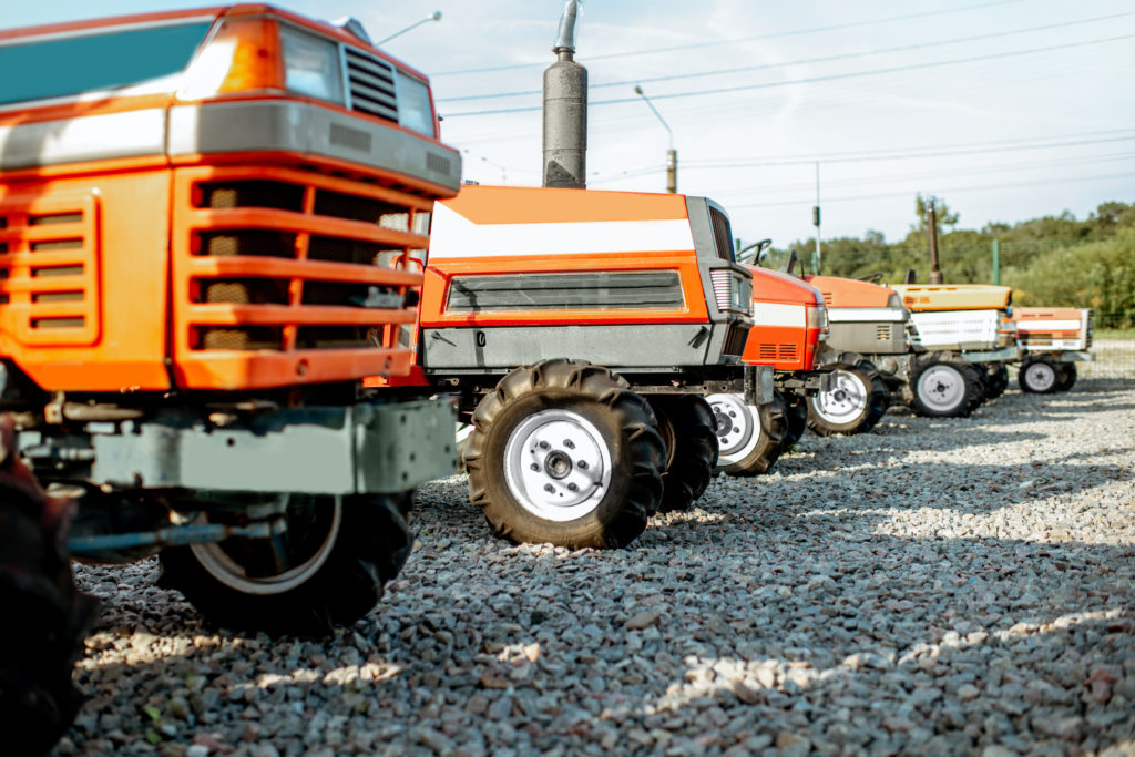Six tractors that are being tracked using IoT software are sitting on a gravel lot.