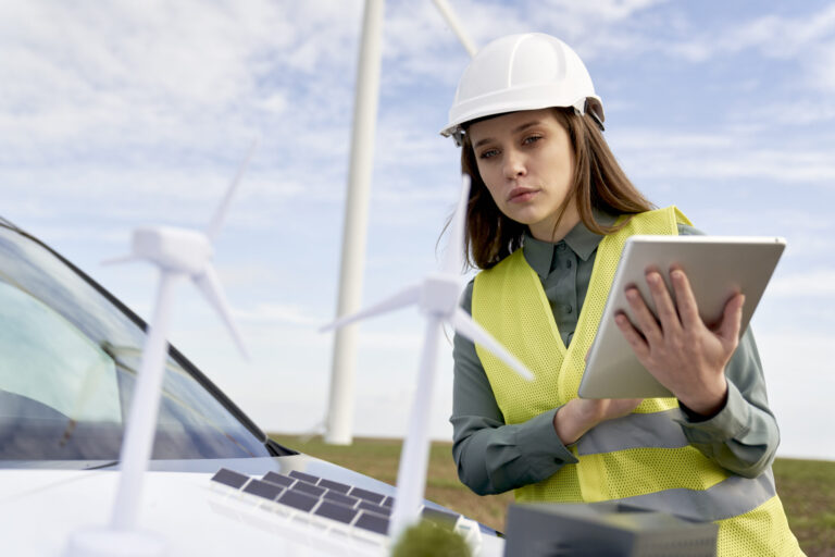 Female caucasian engineer browsing digital laptop and wind turbine field model on car hood