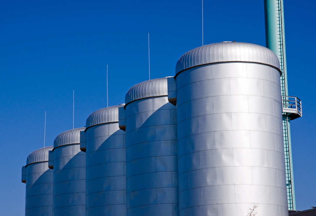 A row of silver IoT monitored industrial tanks against a blue sky.