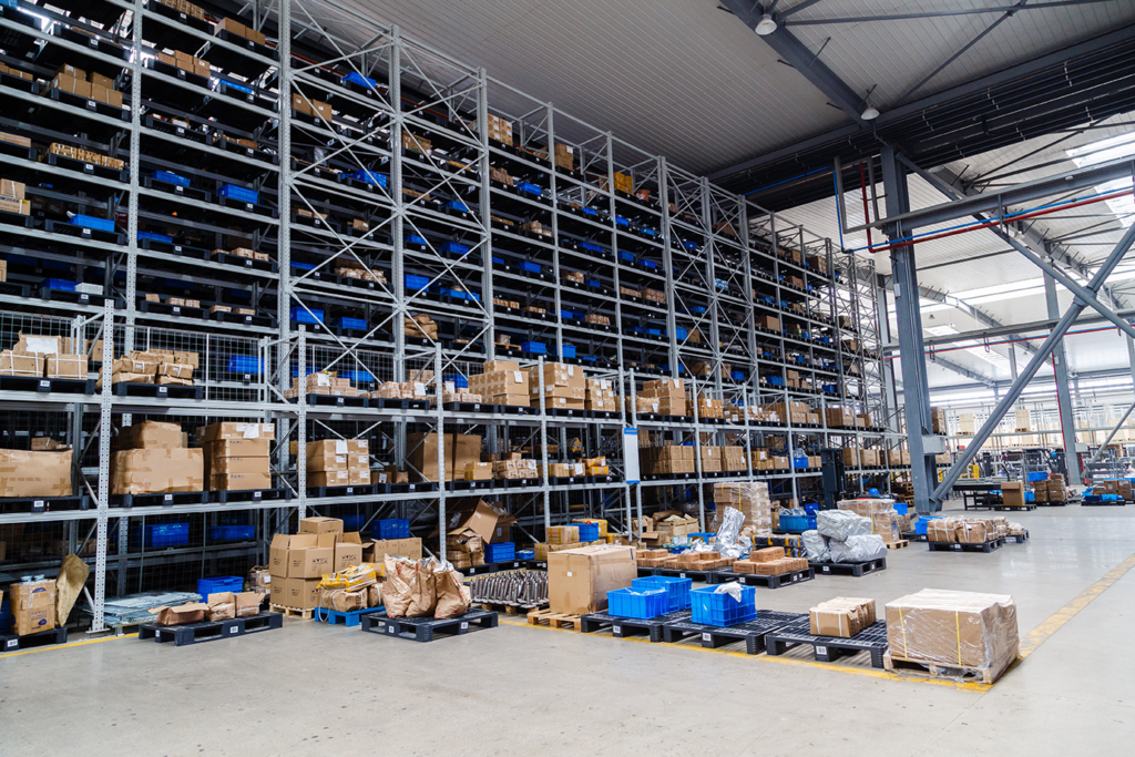 A warehouse with blue containers and cardboard boxes using IoT tracking solutions to help reduce the sting of tariffs.